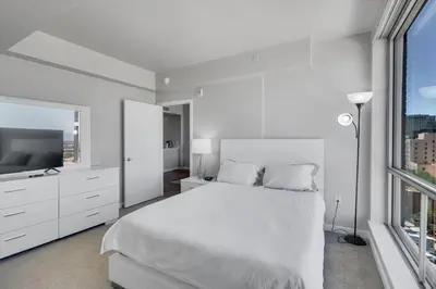 a white bedroom with a bed and a large window at Global Luxury Suites in LA's Seaside in Los Angeles
