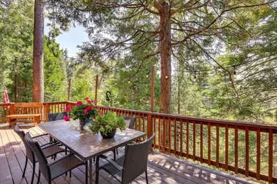 a wooden deck with a table with chairs and flowers at 3 Mi to Lake Arrowhead Village Dog-Friendly Cabin in Lake Arrowhead