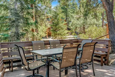 a table and chairs on a deck with trees at Castle Rock Cabin #1 ~ Comfortable cabin with modern amenities and deck - near hiking and lake in Big Bear Lake