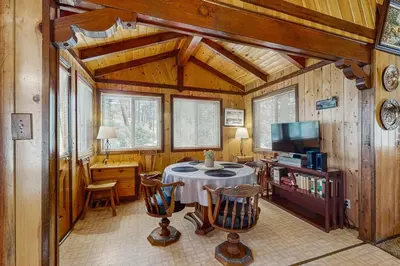 a living room with a table and a tv and wooden walls at Idle Ours Cabin ~ Rustic and Cozy Cabin with Fireplace & Private BBQ - Walk to Big Bear Lake in Fawnskin