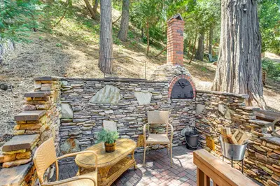 a patio with a stone fireplace and a table and chairs at Forest Views and Fire Pit! Cozy Cabin in Crestline in Crestline