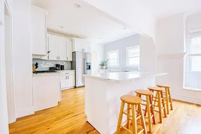 a white kitchen with white cabinets and bar stools at Inviting 3BR Home with Porch & Greenery in Los Angeles