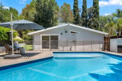 a swimming pool with a white building and an umbrella at Hillside Modern Retreat with pool BBQ and MORE in Los Angeles