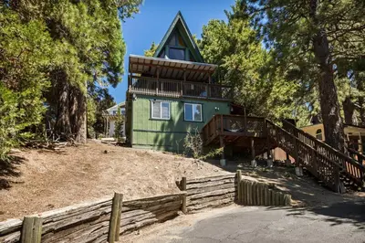 a green house on a hill with a wooden fence at Casa Huntsted A-Frame Cabin near Snow Valley in Running Springs