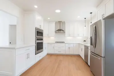 a white kitchen with white cabinets and a refrigerator at Fullerton Adventure Basecamp - Short Trip To Disneyland in Anaheim