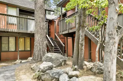 a house with trees and rocks in front of it at Switzerland Summit Condo- Cozy Base Camp Resort Chalet- Walk to Ski Lifts + Hiking in Big Bear Lake