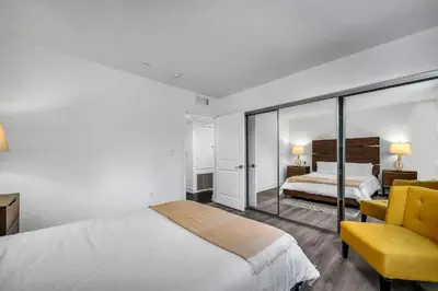 a white bedroom with a bed and a yellow chair at Amazing & Spacious in Heart of Santa Monica- Easy Access to ALL Tourist attractions in Los Angeles
