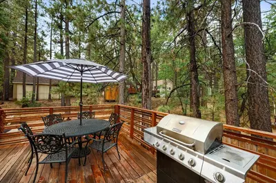 a grill and table on a wooden deck with a table and chairs at Navigate Stays 5BR Group Lodge Near Mountain & Fun in Big Bear Lake