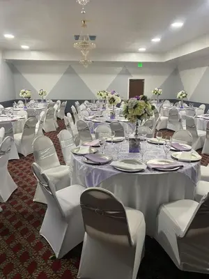 a banquet room with white tables and white chairs at Hiltop Hotel in Bakersfield