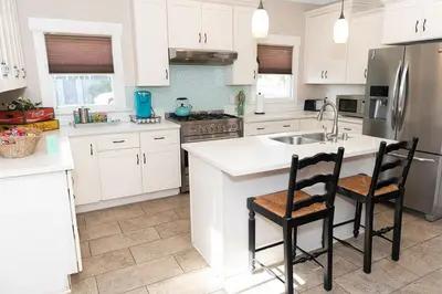 a kitchen with white cabinets and a kitchen island with two chairs at Historic craftsman sleeps 9 3br2.5ba Disney 1mi in Anaheim