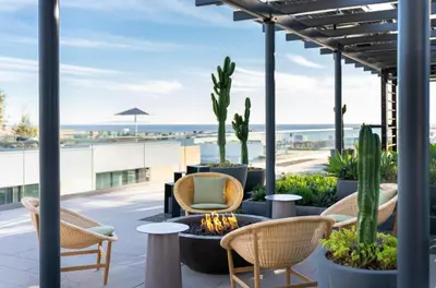 a patio with chairs and a fire pit with a view of the beach at Pearl Coast - Modern 2BR with Rooftop Pool & Views in Los Angeles