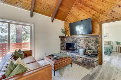 a living room with a stone fireplace and a flat screen tv at Deck and Views Modern Cabin Near Lake Arrowhead! in Lake Arrowhead
