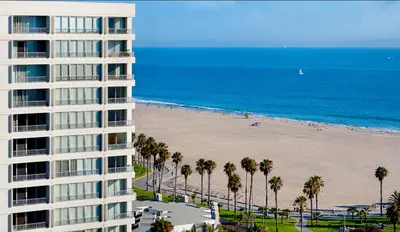 a tall building next to a beach with palm trees at Santa Monica Ocenfront 2 Bedroom Villa with Parking in Los Angeles