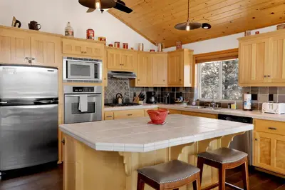 a kitchen with wooden cabinets and a stainless steel refrigerator at View On the Rocks Scenic Mountain Oasis with Hot Tub, Fire Pit and Game Room in Big Bear Lake