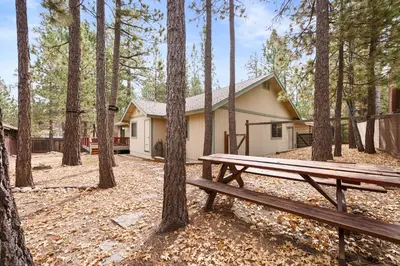 a picnic bench in front of a house in the woods at Leaf & Needle - Walk to Lake & Village, Picnic Table, Single Story, Fenced Yard in Big Bear Lake