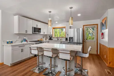 a kitchen with white cabinets and a large island with bar stools at Log Cabin Dream - Log Cabin, Walk to Lake, Fireplace, Deck, BBQ in Big Bear Lake
