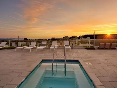 a pool with chairs and the sunset in the background at Luxury 2BD 2BA with Roof Top Pool, Hot Tub & Gym in Los Angeles