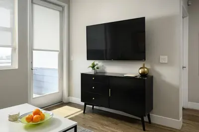 a living room with a black dresser with a television on a wall at The Belladonna at Main Place - Disney Gift Card! in Orange
