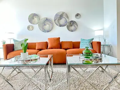 an orange couch in a living room with two glass tables at 5 Star Location with Open City Views 2BD 2BA with King Beds in Los Angeles