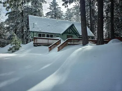 a green house in the snow with trees at Cozy Cabin Retreat with a Hot Tub in Running Springs
