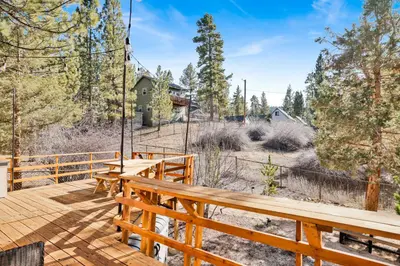 a wooden deck with benches and trees in the background at Sweet Dream Cabin on Dream Street | Walk to Alpine Slide, Dining, & Big Bear Fun in Big Bear Lake