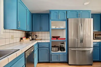 a kitchen with blue cabinets and a stainless steel refrigerator at Solstice Shores Chalet, Hot Tub and Lake Views in Fawnskin