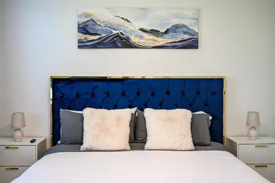 a bed with a blue headboard and a painting on the wall at Charming 3BR Apartment | Near Disney + Arcade in Placentia