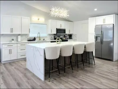 a kitchen with white cabinets and a kitchen island with white bar stools at stunning Poolside villa