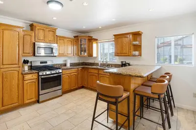 a kitchen with wooden cabinets and a island with bar stools at Family Oasis Near Disneyland & Knotts in Downey
