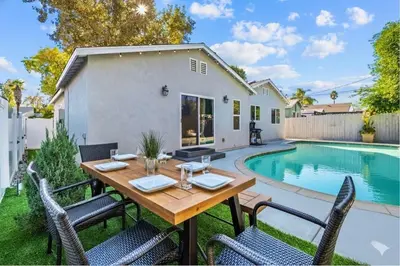 a backyard with a wooden table and chairs next to a swimming pool at Charming Encino Retreat with Pool in Encino