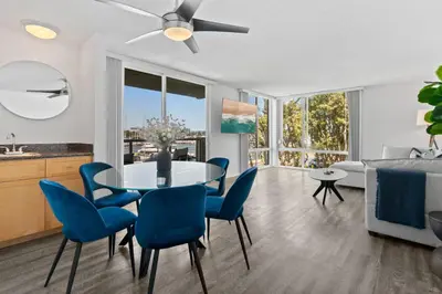a living room with a dining room table and blue chairs at The Glass Anchor - 2 Bed Front-Row Marina Suite in Los Angeles