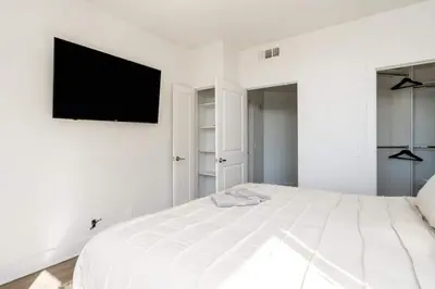 a white bedroom with a bed with a flat screen tv on the wall at Sleek Marina Den, Central, Gym, Pool, King Bed in Los Angeles