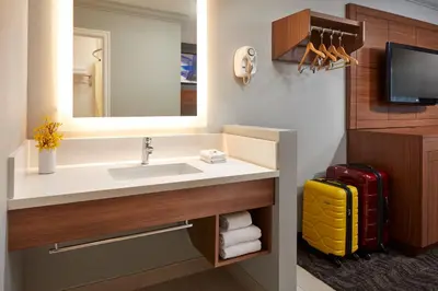 a bathroom with a sink and a mirror and a yellow suitcase at Studio Inn & Suites at Promenade Downey in Downey