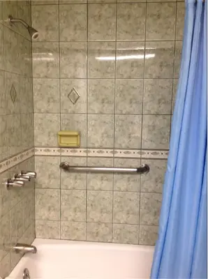 a shower with a blue shower curtain next to a tub at Walls Motel Long Beach in Long Beach