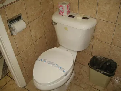 a white toilet in a bathroom with a trash can at Tower Motel Long Beach in Long Beach