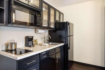 a kitchen with black cabinets and a black refrigerator at Sonesta Simply Suites Anaheim in Anaheim