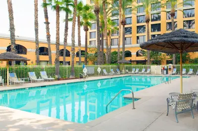a swimming pool with chairs and an umbrella and a building at Delta Hotels by Marriott Anaheim Garden Grove in Anaheim