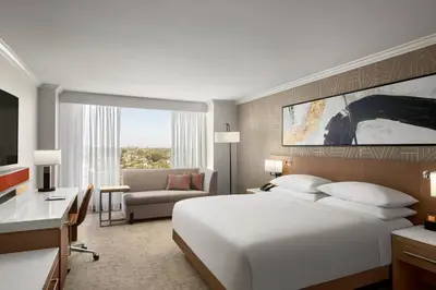 a bedroom with a large white bed and a desk and a room with a desk at Delta Hotels by Marriott Anaheim Garden Grove in Anaheim