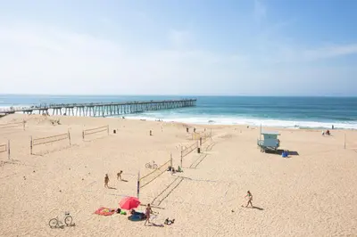 a group of people on a beach with a pier at Beach House Hotel at Hermosa Beach in Hermosa Beach