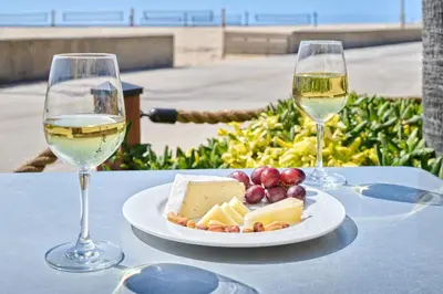 a plate of cheese and grapes and two glasses of wine at Beach House Hotel at Hermosa Beach in Hermosa Beach