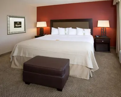 a hotel room with a large bed and a stool at Holiday Inn & Suites Bakersfield by IHG in Bakersfield