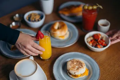 a table with plates of breakfast foods and a person holding a strawberry at The Cove Hotel in Long Beach