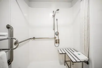 a white bathroom with a bench and a shower at The Buena Park Hotel & Suites in Buena Park