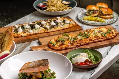 a table topped with pizzas and bowls of food at Burton House, Beverly Hills, A Tribute Portfolio Hotel in Los Angeles