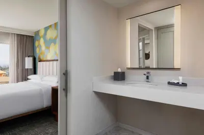 a bathroom with a sink and a mirror and a bed at Anaheim Marriott Suites in Anaheim