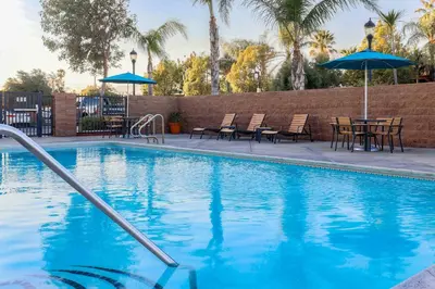 a swimming pool with tables and chairs and an umbrella at Four Points by Sheraton, Ontario-Rancho Cucamonga in Rancho Cucamonga