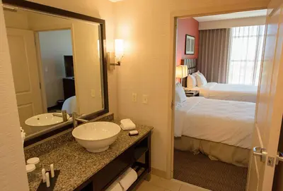 a hotel room with a bed and a sink and a mirror at Embassy Suites Ontario - Airport in Ontario