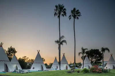 a group of white tents with palm trees in the background at Wigwam Motel in San Bernardino