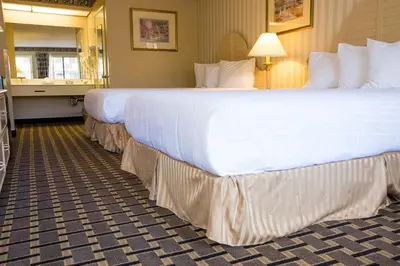a hotel room with two large beds with white sheets at Anaheim Carriage Inn in Anaheim