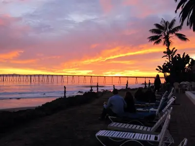 a group of people sitting on the beach watching the sunset at Cliff House Inn in Carpinteria